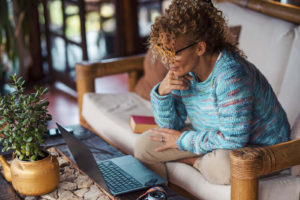 Image of a woman sitting on a couch talking on a laptop for online couples counseling in Colorado. Online therapy is for individuals, couples, and families. Meeting with an online therapist from the comfort of your couch can help make maintaining teletherapy easier. 