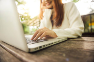Image of a woman in a white sweater sitting outside on a laptop speaking with an online therapist in Colorado. Online therapy or teletherapy in Colorado lets you receive mental health support from anywhere. Including outside in your garden.