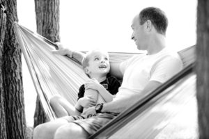 Image of a man sitting in a hammock between trees with his son. Representing the kind of bond you can form with support from a Colorado Springs family therapist. Through family therapy and counseling you can reduce stress and increase connection.