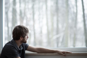 Image of a man looking out a large window into the woods. Representing that getting a psychosexual evaluation or sex offender risk assessment in Colorado Springs, Colorado can help you feel better. By giving you guidance on what steps to take going forward.
