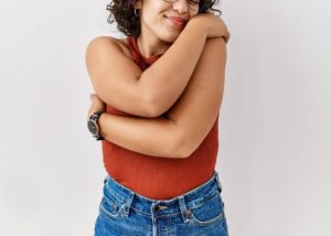 Image of a woman in an orange tank hugging herself. Representing personal mantras are taught in anxiety therapy. You can get body image anxiety help in Colorado Springs, CO.