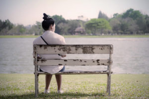 Image of a woman sitting alone on a bench. Representing the feelings that can accompany traumatic grief and how online therapy with a trauma therapist in Colorado Springs, CO can help.