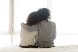 A mother hugs their teen while sitting at the end of a bed. Learn more about teen therapy in Colorado Springs, CO, and the support a therapist for teenagers in Colorado Springs, CO can offer. Search counseling for teens near me today. 