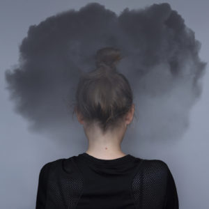 A woman stands looking away from the camera with a cloud around her head. This could represent the struggle of depression symptoms that a Colorado Springs depression therapist can address. Learn more about depression treatment in Colorado Springs, CO